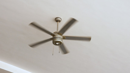 Ceiling fan is rotating at the ceiling of the room. Electric climate equipment.