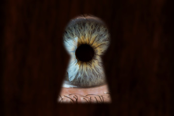 Male blue eye looking through the keyhole. Concept of voyeurism, curiosity, Stalker, surveillance...
