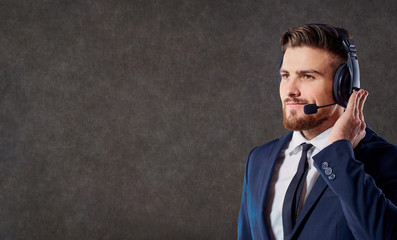 A male call center operator with headset on his head answers calls on the office background.