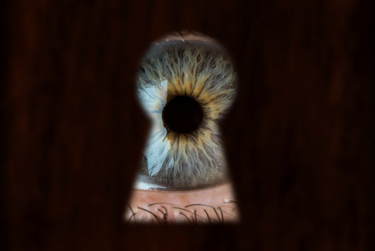 Male blue eye looking through the keyhole. Concept of voyeurism, curiosity, Stalker, surveillance and security