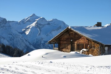 Facade of a old timber hut and snow covered mount Oldenhorn. Winter scene near Gstaad, Switzerland.