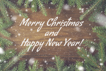 Christmas congratulation text on wooden background with pine or fir green branches and snow.