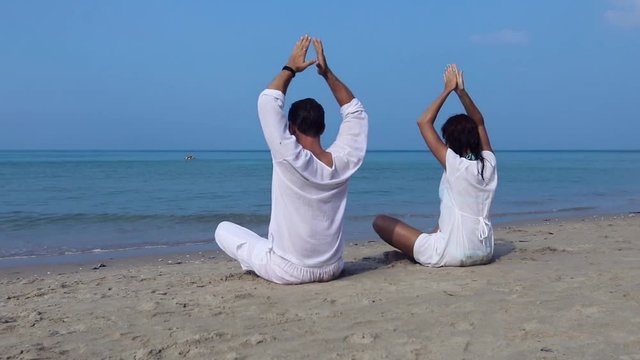 Two people with white clothes practicing movements of yoga lotus position on the beach during warm summer vacation, meditation, spirituality and well being