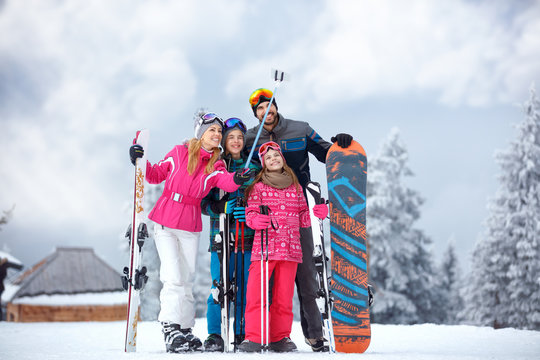 Skiing family enjoying winter vacation on snow in cold day and making mobile selfie