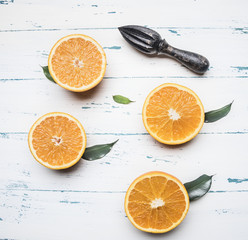 fresh sliced oranges with leaves and wooden crush for fruit, on rustic wooden background, top view