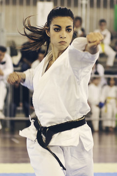 A black belt girl is performing a kata at a karate competition. People out of focus in background.