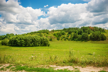 Green grass field on small hills and blue sky with clouds