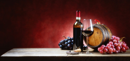 Red wine glass with bunches of grapes, bottle and small barrel