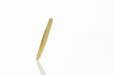 Close up isolated gold tweezers on white background with a reflection 