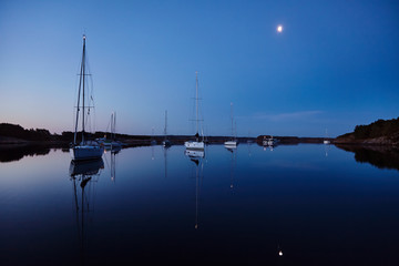 Sailboats illuminated at night anchored in quiet summer evening