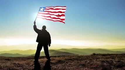 Successful silhouette man winner waving Liberia flag on top of the mountain peak, Cinemagraph LOOP background