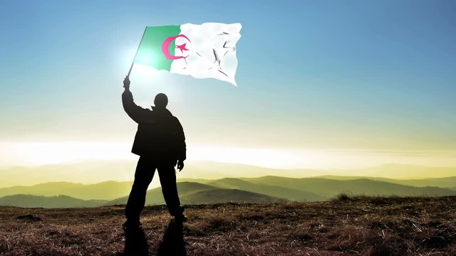 Successful silhouette man winner waving Algeria flag on top of the mountain peak. Cinemagraph LOOP background
