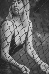 beautiful young woman poses sensually near a metal mesh