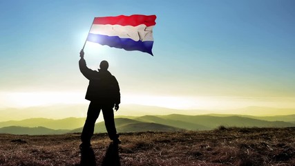 Successful silhouette man winner waving Netherlands flag on top of the mountain peak, Cinemagraph LOOP background - Powered by Adobe