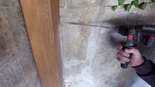 Man’s hands holding electric drilling machine and drilling hole in a concrete wall