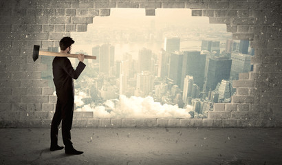 Business man hitting wall with hammer on city view