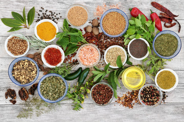 Spice and herb seasoning with fresh and dried herbs and spices, including chili pepper selection, mustard powder and seeds, ground and whole peppercorns and olive oil on rustic wood. Top view.