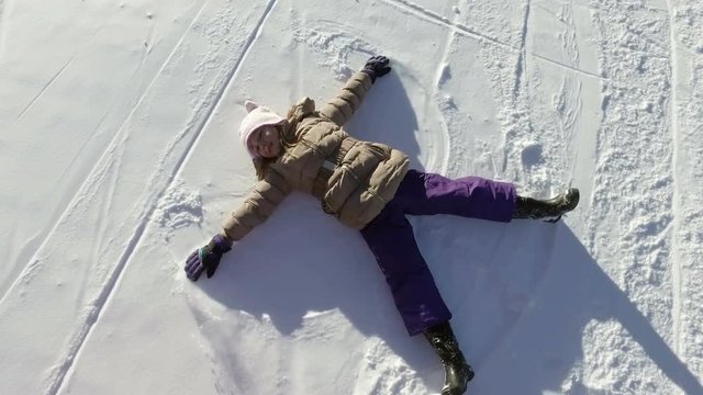 Winter happy girl child lying on snow playing having fun making snow angels