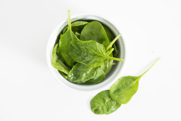 Fresh wet green baby spinach leaves in a bowl, closeup on white background.