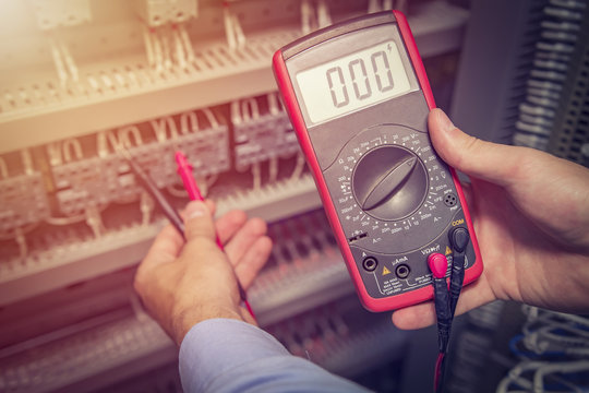Service engineer with multimeter tester in hands close up. Electrical measurements in electric cabinet. Support specialist with test device