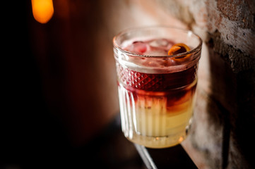 Glass of red and white alcoholic cocktail with a slice of orange peel