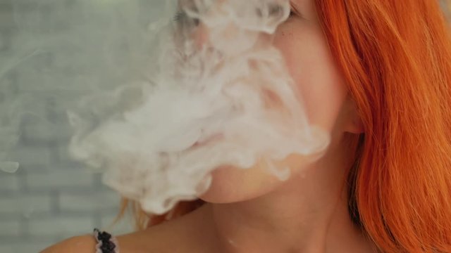 Cute red hair young woman with vape at light room