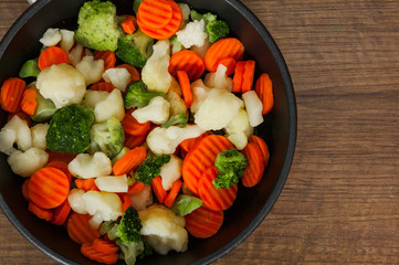 Mixed vegetables. cauliflower, broccoli and carrots in an iron pan on a wooden background. with copy space. top view