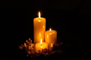 Three candles in a dark room with dried nuts and flowers surrounding them