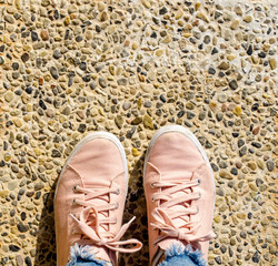 Fototapeta premium Young Woman feet in pink sneakers and in jeans on cobbled stony road