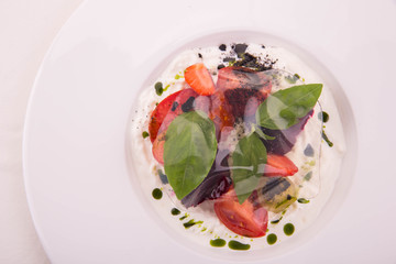 Sweet tomatoes with cheese of a stachatell, young beet, strawberry and a basil, is served with ornament from transparent tomato water jelly