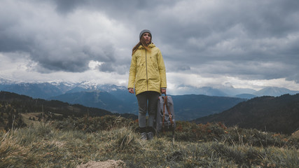 Hipster young girl with backpack hiking in mountains. Tourist traveler walking on top of the mountain