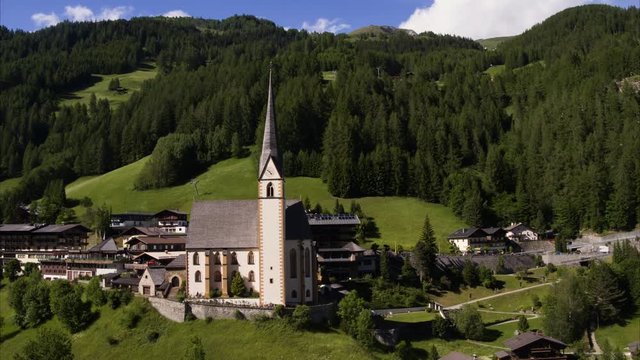 Wide aerial panning shot of tower in rural valley town / Heiligenblut, Austria