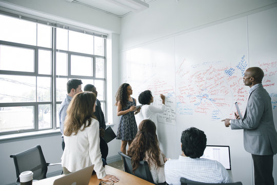 Businesswoman writing on whiteboard in meeting - Powered by Adobe