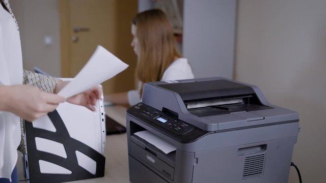 woman in an office is taking papers from printer, working day in sales department of a small business company