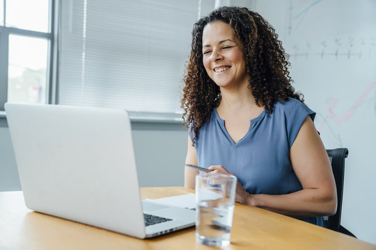 Mixed race businesswoman smiling at laptop