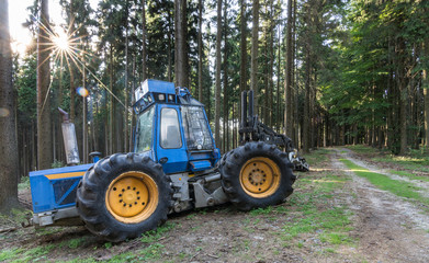 Blue harvester in a sunny summer wood. Industrial background with logging machine next to a forest...