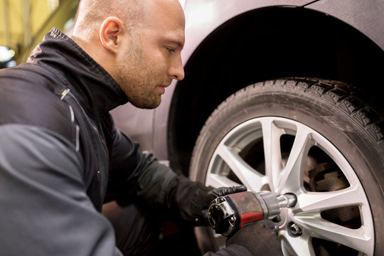 auto mechanic with screwdriver changing car tire