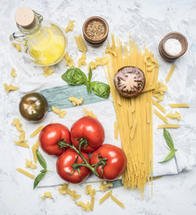 preparation of appetizing Italian pasta, with tomatoes, basil, and oil in a decanter, spices and seasonings on a white rustic background, top view