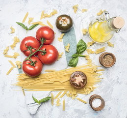 preparation of appetizing Italian pasta, with tomatoes, basil, and oil in a decanter, spices and seasonings on a white rustic background, top view