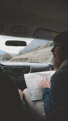 Fototapeta premium Rear view shot of couple traveling by car. Woman holding map, laughing and smiling. Couple on a road trip.