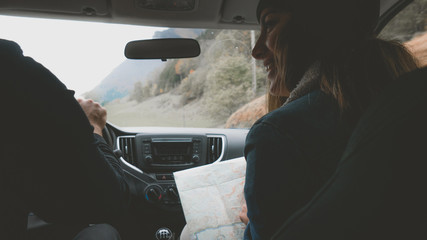 Rear view shot of couple traveling by car. Woman holding map, laughing and smiling. Couple on a road trip.