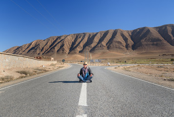 Woman sitting with cross leg on the road. Fork in the road. Morocco