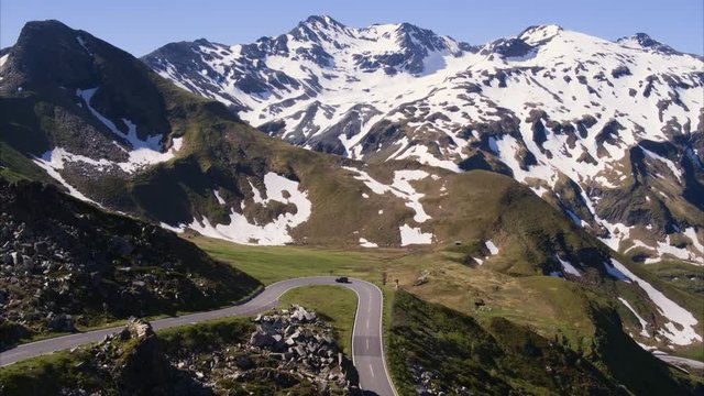 Wide aerial shot of car driving on curving mountain pass / Grossglockner, Austria