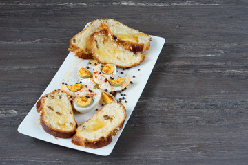 Sliced Easter bread and eggs in white plate on grey wooden board.