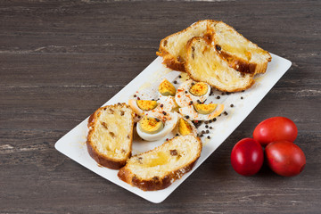 Easter colored eggs and sliced Easter bread in white plate on grey wooden board.