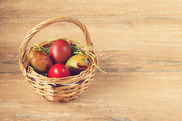 Easter wicker basket with colored eggs on brown wooden board.