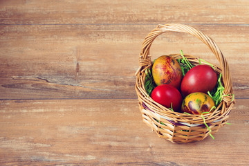 Easter wicker basket with colored eggs on brown wooden board.