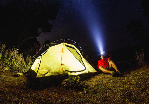 Man hiker with flashlight near his camp tent at night in fog