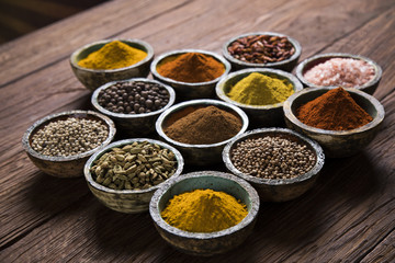 A selection of various colorful spices on a wooden table in bowls