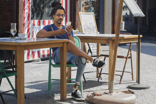 Mixed race man with prosthetic leg texting on cell phone at sidewalk cafe